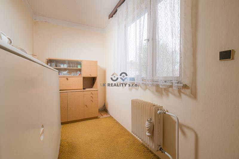 Ein Zimmer in einem Einfamilienhaus mit älteren Möbeln, einem Heizkörper und einem Teppich.