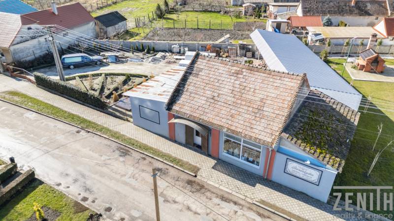 Geschäftsräume in Okoč mit traditionellem Dach, Gehweg und Garten.