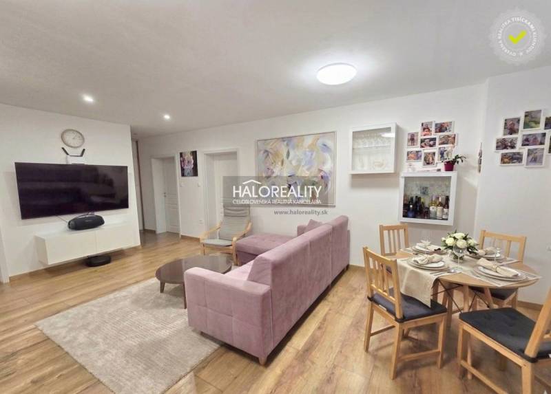 Wohnzimmer in einer 3-Zimmer-Wohnung mit Fernseher, rosa Sofa und Tisch.