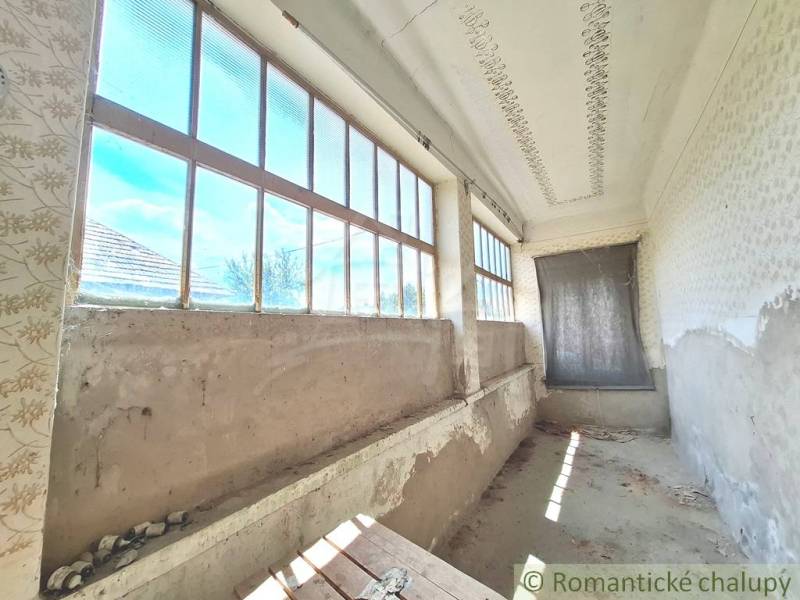 Ein Ferienhaus in Kamenný Most mit einer langen Veranda und großen Fenstern, das renoviert werden muss.