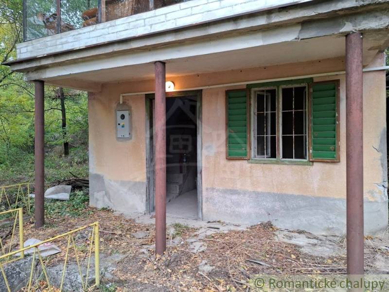 Eine Hütte in Kamenín mit einer Veranda und grünen Fensterläden, umgeben von Natur.