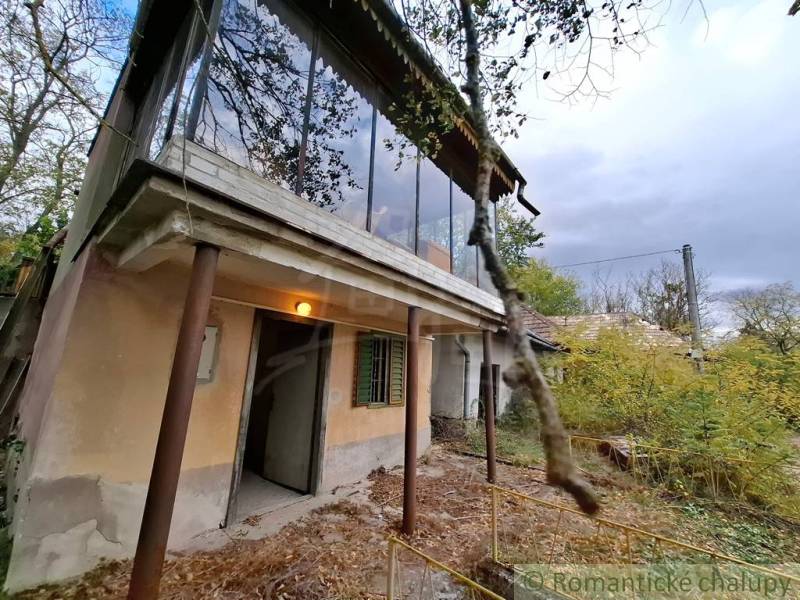 Ein Ferienhaus in Kamenín mit einem verglasten Balkon, umgeben von Natur und einem überwucherten Hof.
