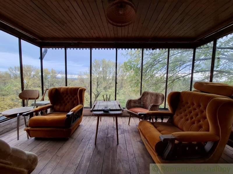 Interieur einer Hütte mit bequemen Sesseln und Blick auf Bäume durch große Fenster.