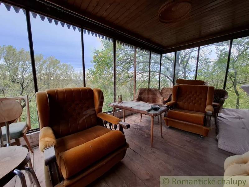 Eine Veranda mit Stühlen und einem Boden in Holzoptik, eine Hütte umgeben von Grün.