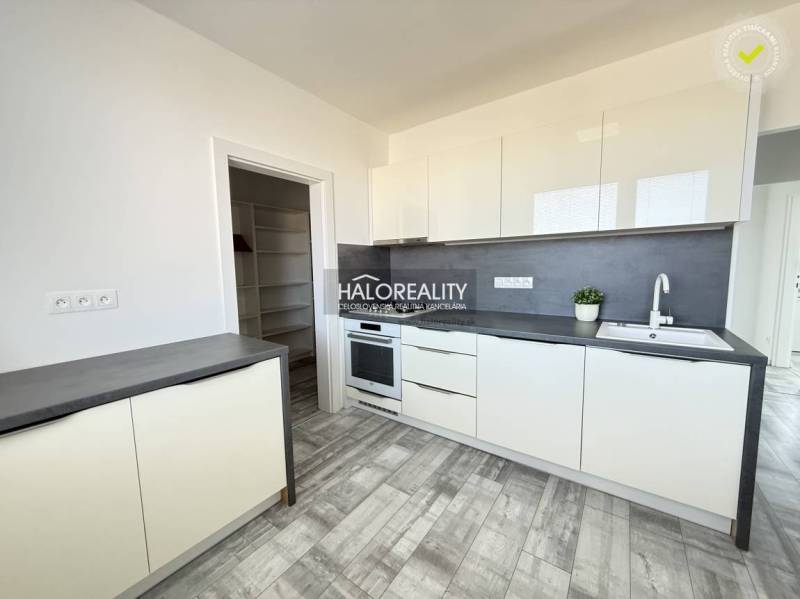 Küche in einer 2-Zimmer-Wohnung mit weißen Möbeln und einem Boden in Holzoptik.