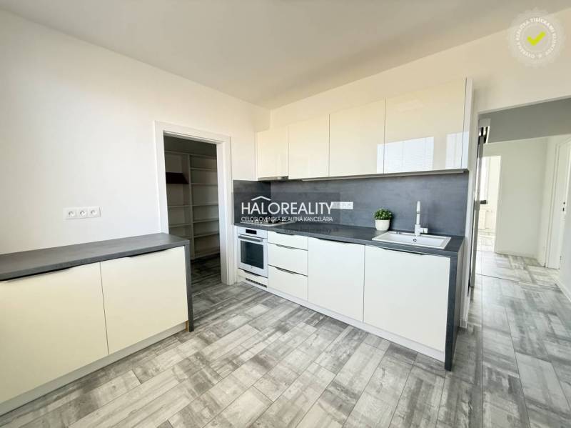 Küche in einer 2-Zimmer-Wohnung mit weißen Schränken und einem Boden in Holzoptik.