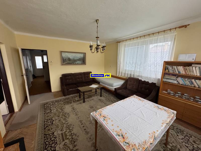 Wohnzimmer in einem Einfamilienhaus mit Sofa, Bücherregal und Tisch mit Tischdecke.