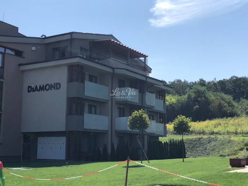 Ein 2-Zimmer-Wohnung in Podhájska, umgeben von Grünflächen und einem wolkenlosen Himmel.