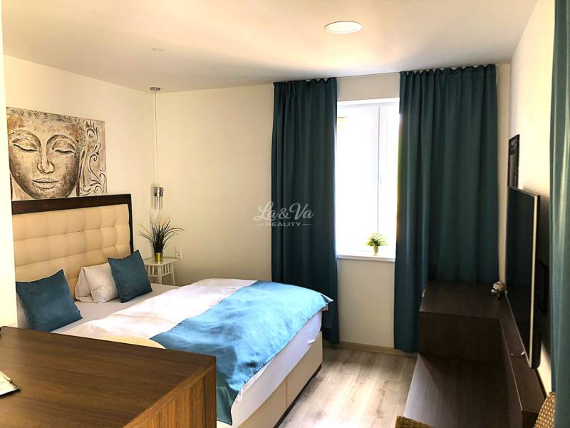 Einzimmerwohnung mit hellen Möbeln, Bett und blauen Vorhängen, Boden mit Holzdekor.