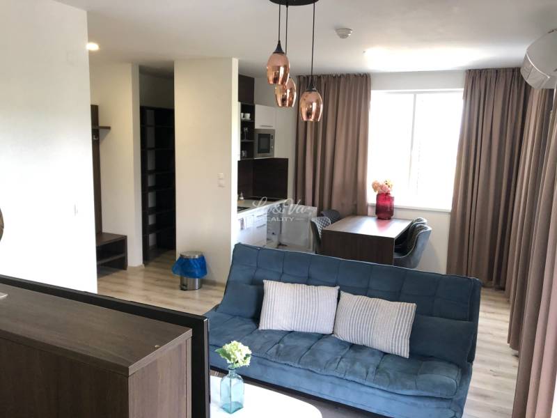 Wohnzimmer in einer Zweizimmerwohnung mit Sofa und Esstisch; Boden mit Holzdekor.