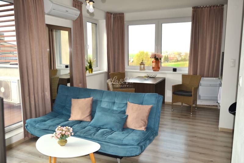 Wohnzimmer mit Sofa, Tisch, Pflanzen und Holzboden in einer Zweizimmerwohnung.