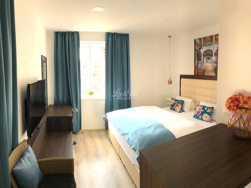 Helles Zimmer in einer 2-Zimmer-Wohnung mit blauen Vorhängen und Holzboden.