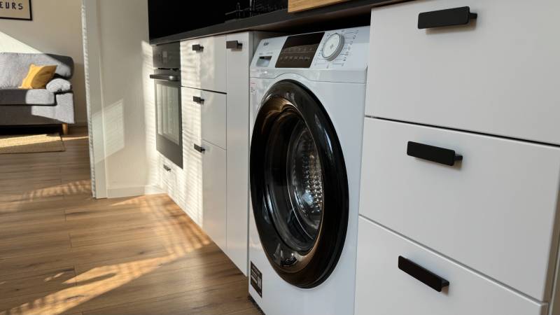 Küche in einer Einzimmerwohnung mit eingebauter Waschmaschine und Boden mit Holzdekor.
