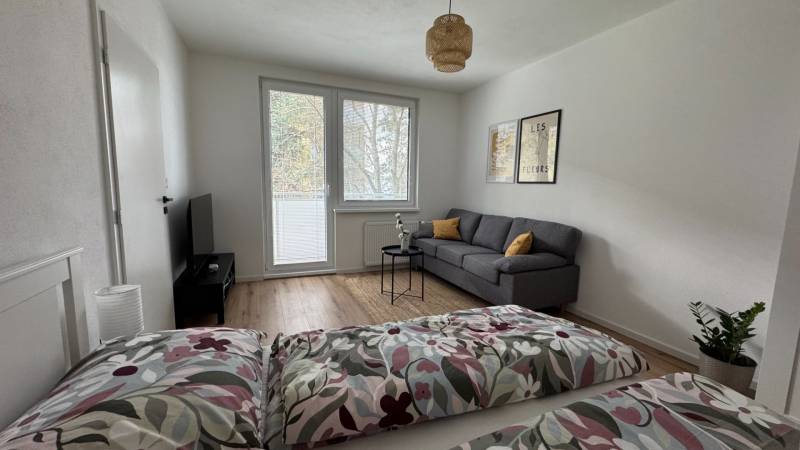 Wohnzimmer in einer Einzimmerwohnung mit Sofa und Fernseher, Boden mit Holzdekor.