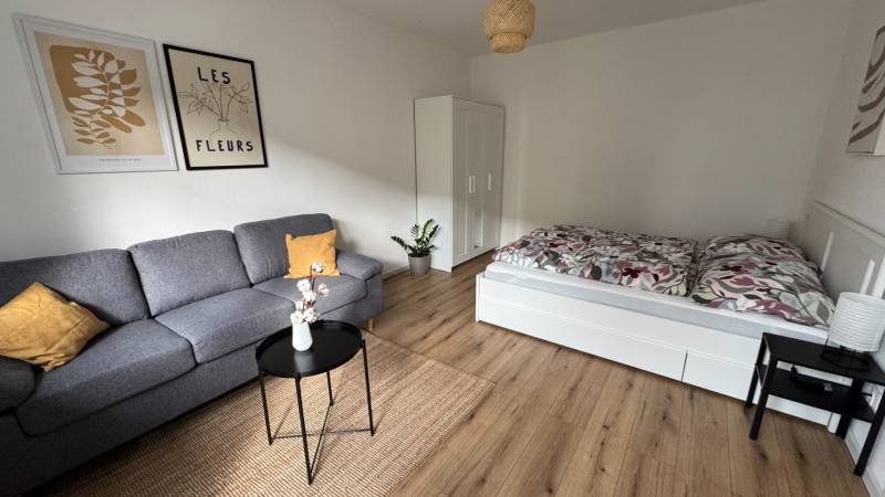 Wohnzimmer in einer Einzimmerwohnung mit Sofa, Bett und Holzboden.