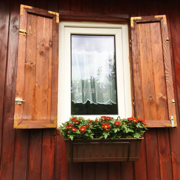 Ein Fenster eines Einfamilienhauses in Bohdanovce nad Trnavou mit Fensterläden und einem Blumenkasten mit roten Blumen.