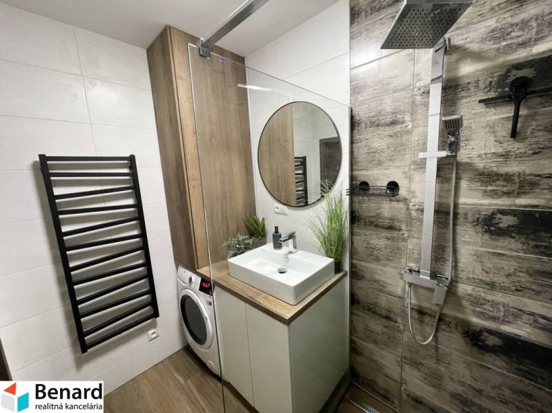 Badezimmer in einer 2-Zimmer-Wohnung mit Waschbecken, Dusche und Waschmaschine, Boden mit Holzdekor.