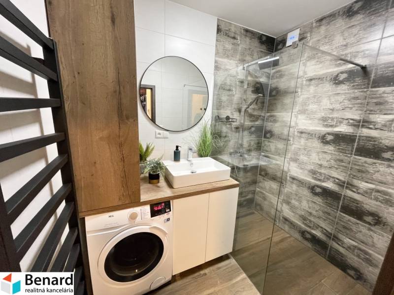 Badezimmer mit Duschkabine, Waschbecken, Waschmaschine und Boden mit Holzdekor in einer 2-Zimmer-Wohnung.