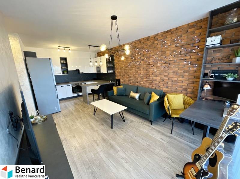 Wohnbereich einer 2-Zimmer-Wohnung mit Ziegelwand, Holzboden und Küchenzeile.