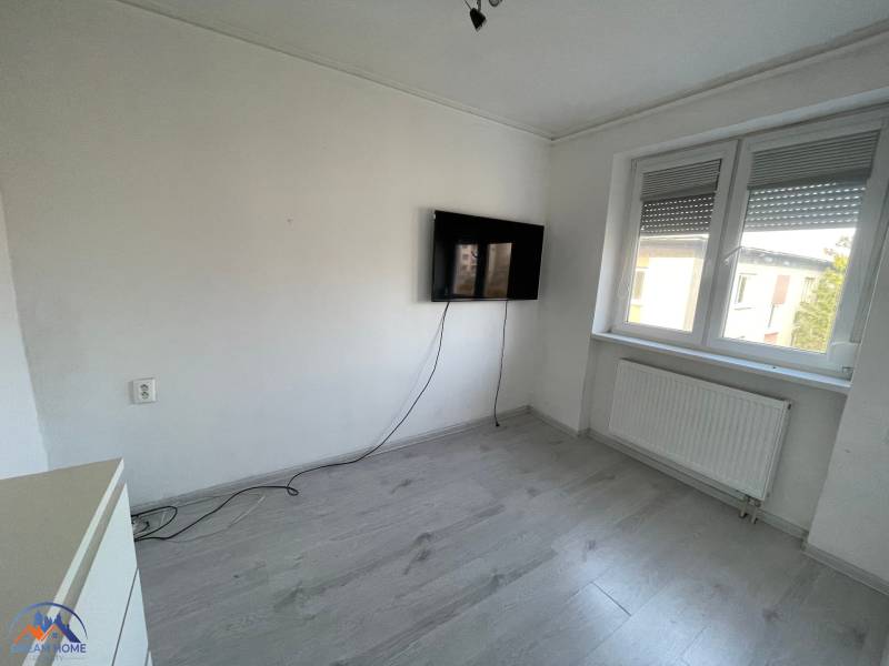 Ein Zimmer in einer 3-Zimmer-Wohnung mit einem Fernseher, einem Boden in Holzoptik und weißen Wänden.