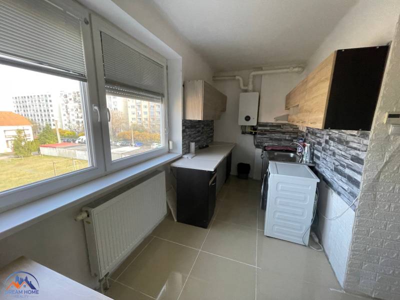 Eine Küche mit einem großen Fenster, einem Heizkörper und einer Küchenzeile in einer 3-Zimmer-Wohnung.