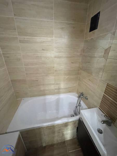 Badezimmer in einer 3-Zimmer-Wohnung mit einer Porzellanbadewanne und Fliesen in Holzoptik.