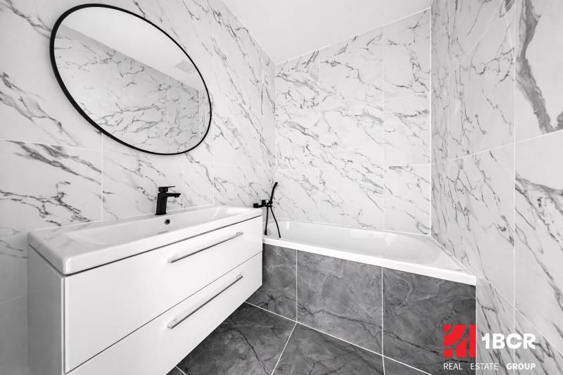 Badezimmer mit Marmorfliesen, ovalem Spiegel und modernem Waschbecken in einer 3-Zimmer-Wohnung.