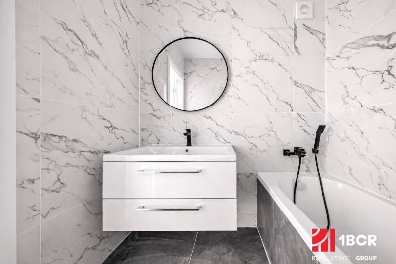 Badezimmer in einer 3-Zimmer-Wohnung mit Marmorfliesen, Waschbecken und Spiegel.