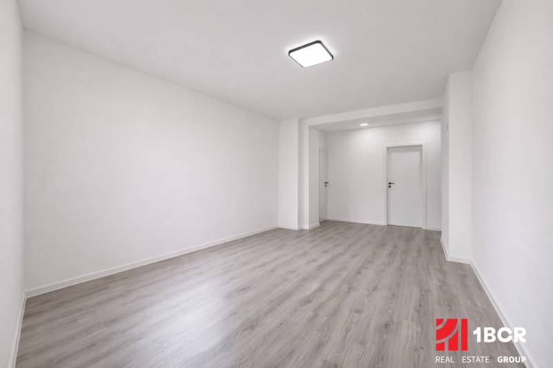 Ein geräumiges Zimmer in einer 3-Zimmer-Wohnung mit einem Boden in Holzoptik und weißen Wänden.