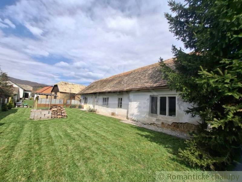 Ein Einfamilienhaus in Ozdín mit ursprünglichem Aussehen und einem grasbewachsenen Hof, umgeben von Bäumen.