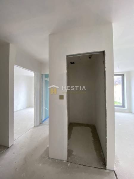 Innenraum einer unvollendeten 2-Zimmer-Wohnung mit verputzten Wänden und einem großen Fenster.