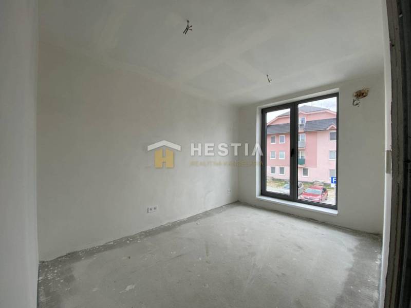 Ein Zimmer in einer 2-Zimmer-Wohnung mit rohem Boden und einem großen Fenster mit Blick auf die Straße.
