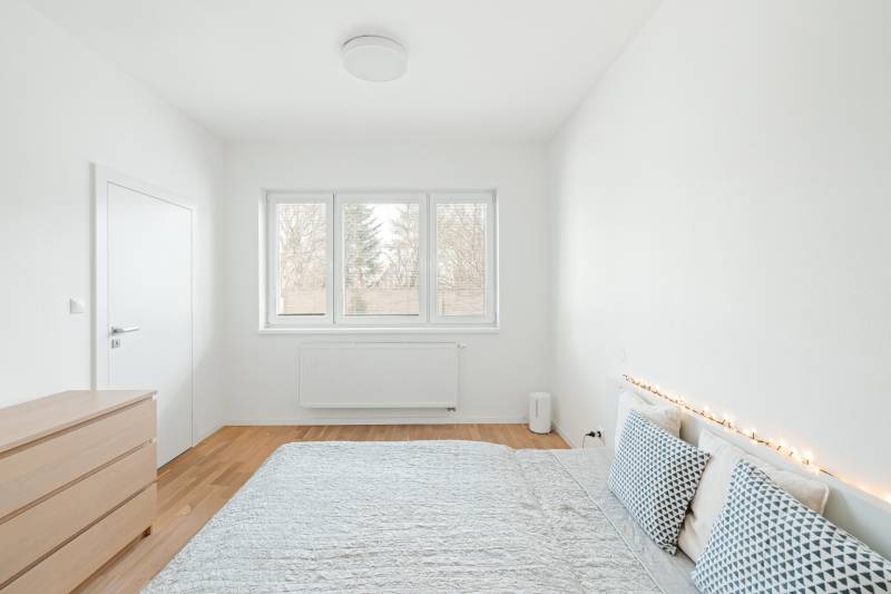 Helles Schlafzimmer in einer Vierzimmerwohnung mit Holzboden und dekorativen Kissen.