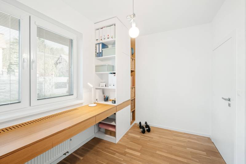 Ein Arbeitszimmer mit einem Holztisch und Regalen in einer Vierzimmerwohnung, Boden mit Holzdekor.