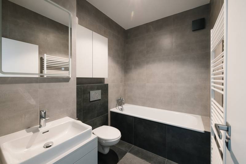 Badezimmer mit Badewanne, Waschbecken und Toilette in einer 4-Zimmer-Wohnung, stilvolle graue Fliesen.