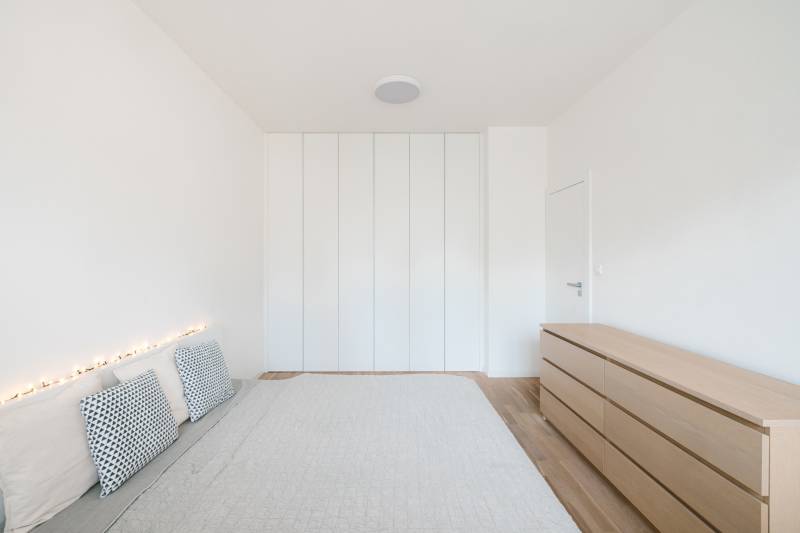 Helles Schlafzimmer in einer 4-Zimmer-Wohnung mit Bett, Kissen und Schrank, Boden mit Holzdekor.