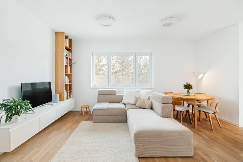 Wohnzimmer mit Sofa, Fernseher, Bücherregal und Esstisch, Boden mit Holzdekor.