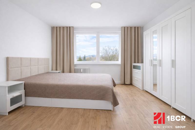 Schlafzimmer mit Doppelbett, Schrank und Holzboden in einer Zweizimmerwohnung.