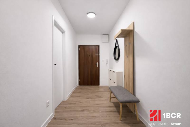 Der Flur einer 2-Zimmer-Wohnung mit einem Boden in Holzoptik, einem Spiegel und einer Bank.