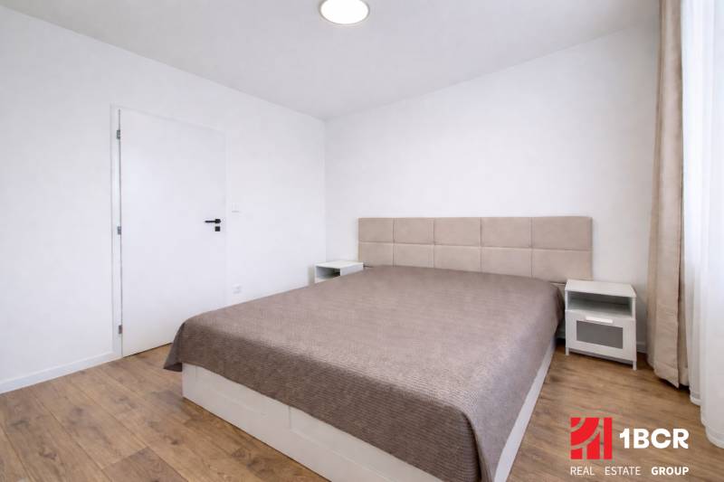 Schlafzimmer in einer 2-Zimmer-Wohnung mit einem großen Bett und einem Boden in Holzoptik.