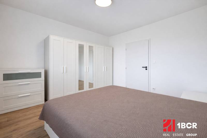 Schlafzimmer mit weißem Schrank und Kommode in einer 2-Zimmer-Wohnung, Boden mit Holzdekor.