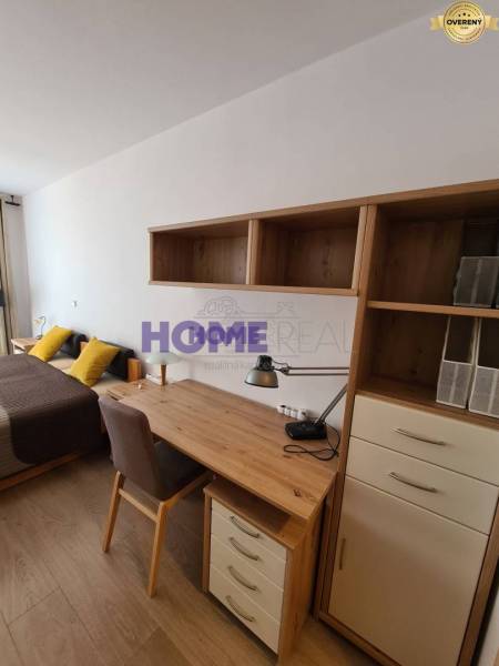 Schreibtisch mit Regalen, Bett und Boden mit Holzdekor in einer 2-Zimmer-Wohnung.