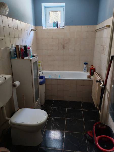 Badezimmer mit Badewanne und Toilette in einem Einfamilienhaus, mit dunklen Fliesen und einem Fenster.