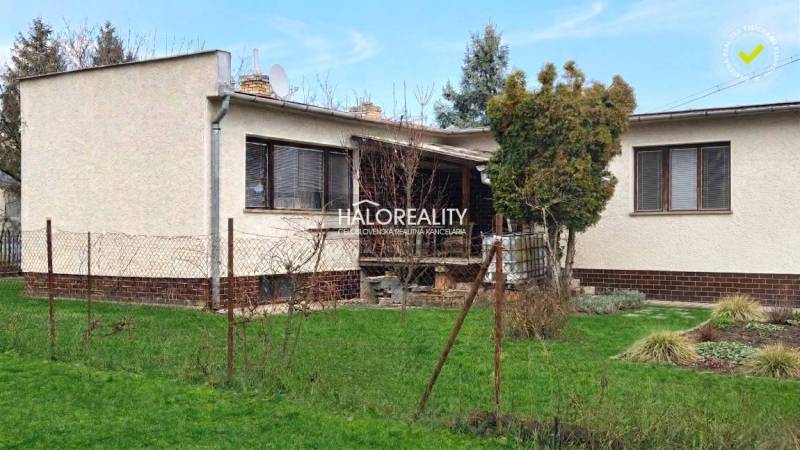 Ein Einfamilienhaus in Poltár, umgeben von Rasen und Bäumen, mit Terrasse und Zaun.