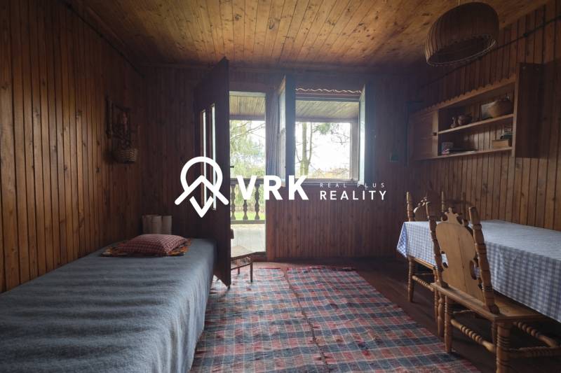 Innenraum einer Hütte mit Holzeinrichtung, Bett, Tisch, Stühle und Teppich.