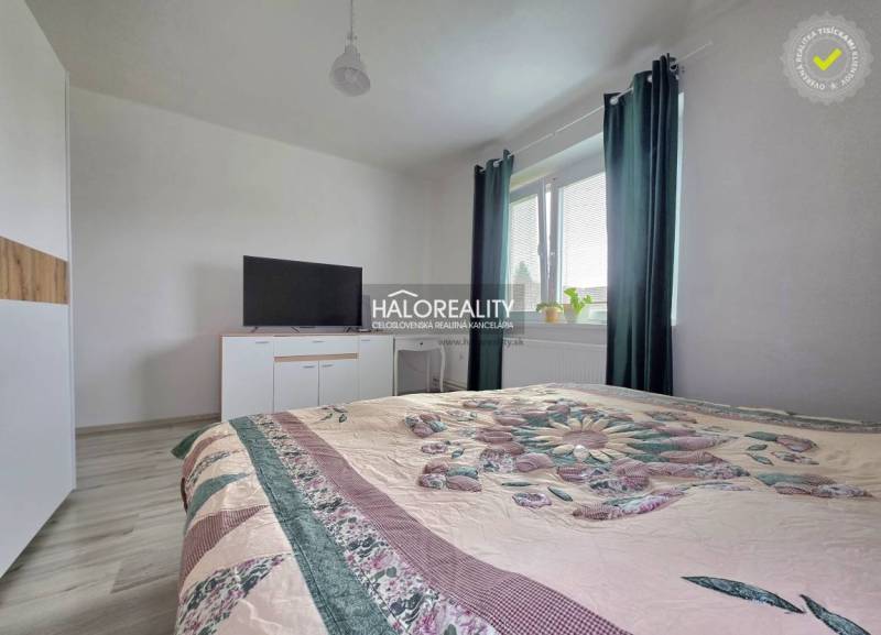 Schlafzimmer in einem Einfamilienhaus mit Bett, Fernseher und Fenster mit dunklen Vorhängen.