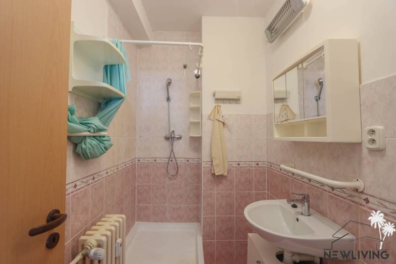 Badezimmer in einer 2-Zimmer-Wohnung mit rosa Fliesen, Waschbecken und Duschkabine.