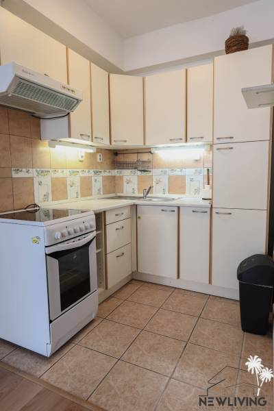 Küche in einer 2-Zimmer-Wohnung mit weißen Schränken und Herd, Boden mit Holzdekor.