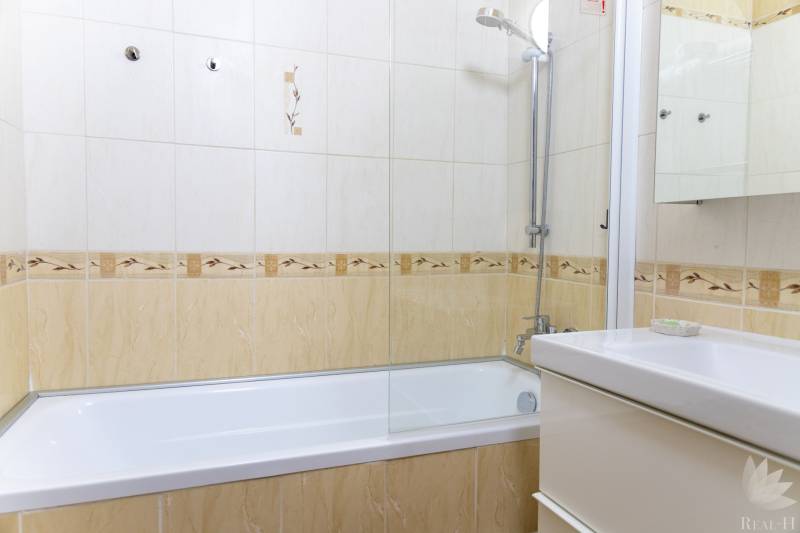Badezimmer mit Fliesen und Badewanne in einer 4-Zimmer-Wohnung, helle Farben und Duschkopf.