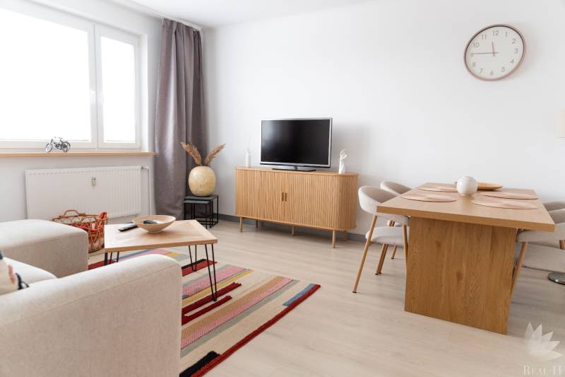 Wohnbereich einer 4-Zimmer-Wohnung mit Fernseher, Sofa, Tisch und Boden in Holzoptik.